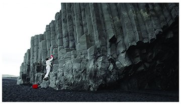 Judy Natal: video still from The Custodian. A person is washing the side of a cliff with a bucket of water and a wash cloth.