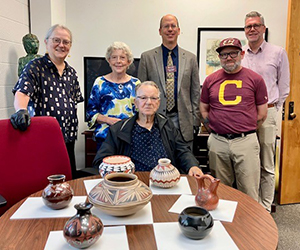 Members of the College of the Arts and Media sit with Jerry and Marry Thompson. His pottery collection is on a table in front of them.