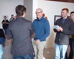 Larry Burditt attending an art exhibit at the University Art Gallery. He is shaking the hand of another attendee.