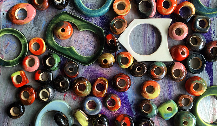 An array of ceramic beads of all shapes and sizes and colors laid out on a painted wood table.
