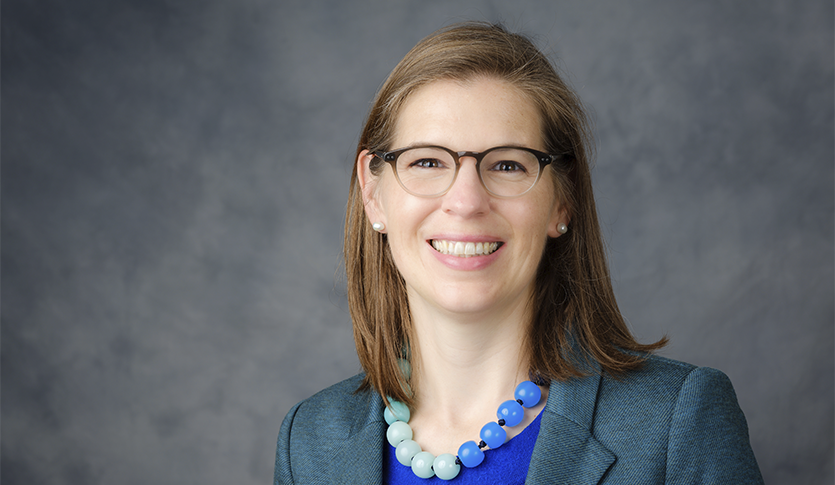 Headshot of Morna O'Neill. She is wearing a grey blazer with a blue, large beaded necklace.