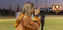 Photojournalism student Alivia Cranick taking photos on the field at a soccer game