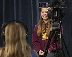 Journalism student Ella Pierzecki telling a news story in front of a camera in the MHTV studio