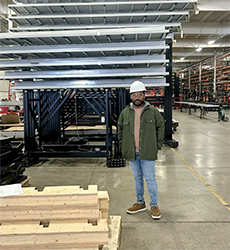 Graduate student Sashi Maddikunta standing in a lumber warehouse, wearing a hard hat and protective eyewear