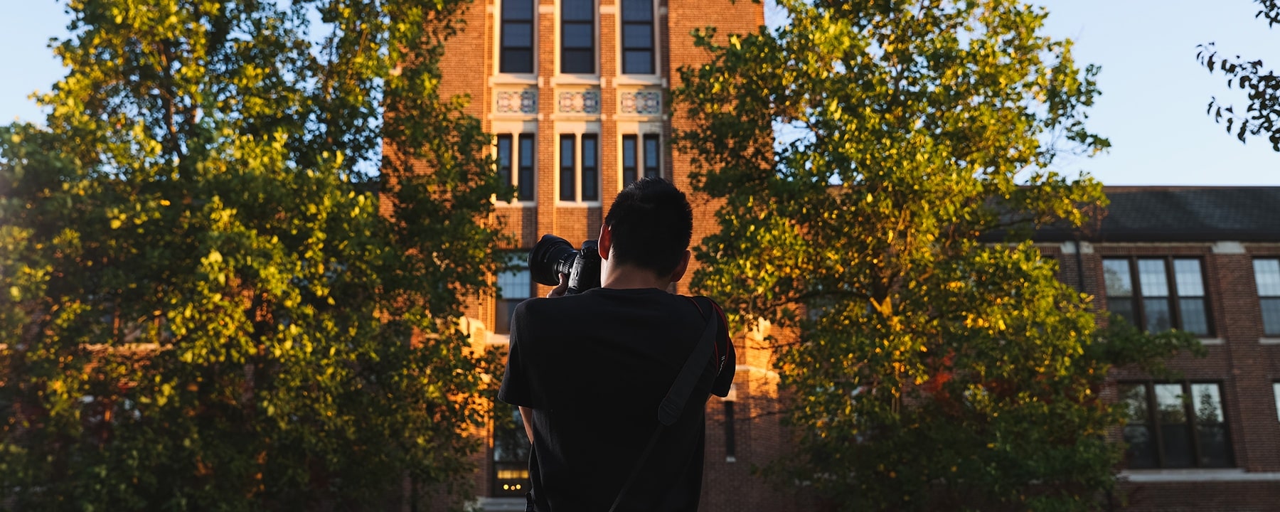 College of Art and Media photojournalism student taking picture on the campus of Central Michigan University in front of Warriner Hall.