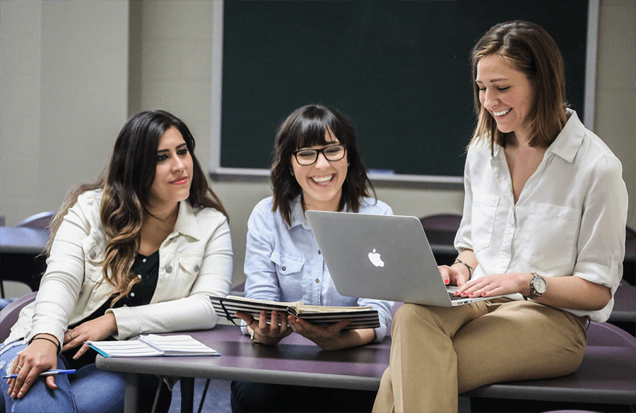 Three journalism alumni meeting with a laptop.