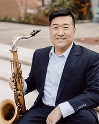 Headshot of Jordan VanHemert. He is sitting on stone steps with his saxophone at his hip.