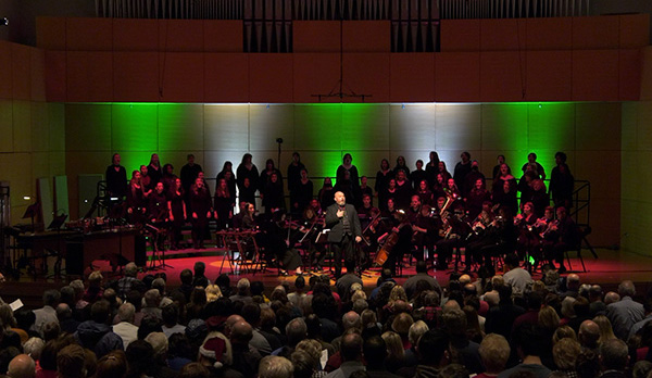 2022 Juletide performers wearing all black under green and white lights on stage at Staples Family Concert Hall