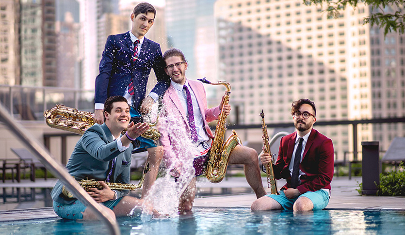 The Nois saxophone quartet posing with their instruments in a pool with a cityscape in the background.
