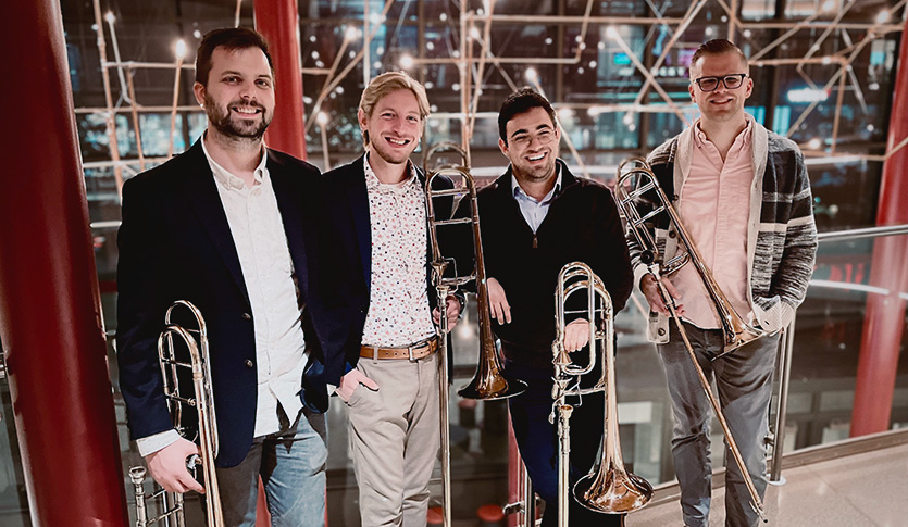 Members of The Beltline Bones quartet stand with their trombones in front of a metal framework.