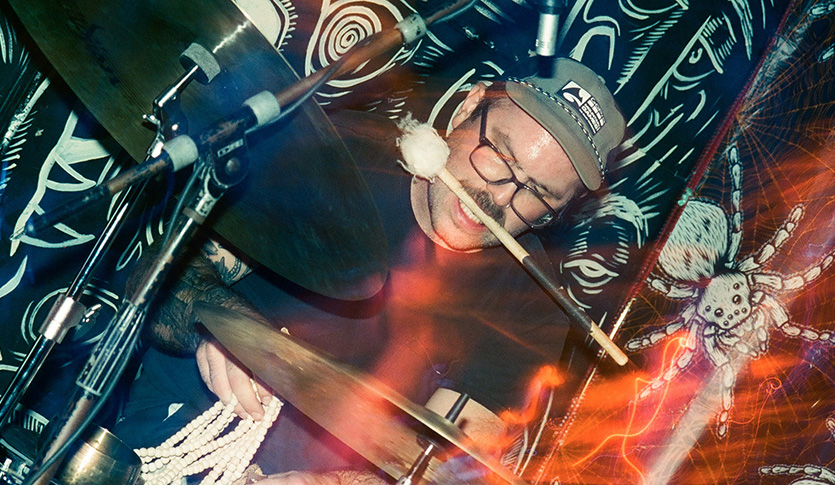 Percussionist Sean Hamilton playing drum set in a punk-style room.