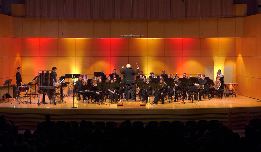 A picture of the CMU Wind Symphony performing on stage in Staples Family Concert Hall under the direction of Dr. Batcheller.
