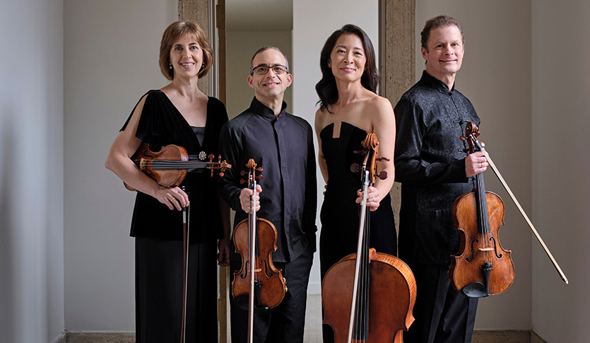 The Brentano String Quartet posing in a grey room.