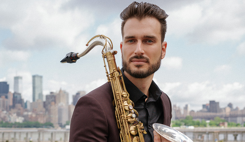 Chad LB holding his saxophone with a city skyline in the background