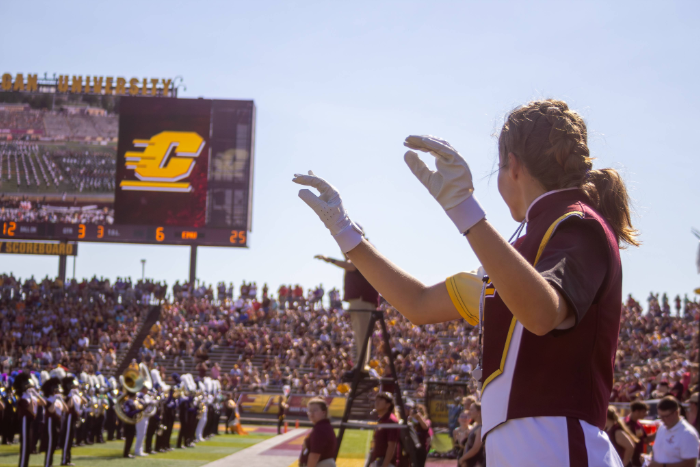 a drum major conducting in front of marching band with CMU Action C in the background