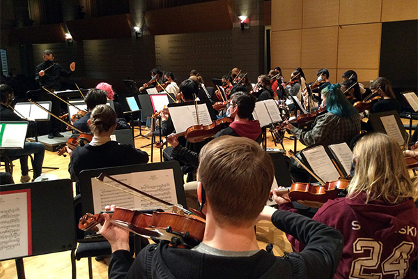 The 2021 Central Michigan University Honors String Orchestra students rehearse on stage.
