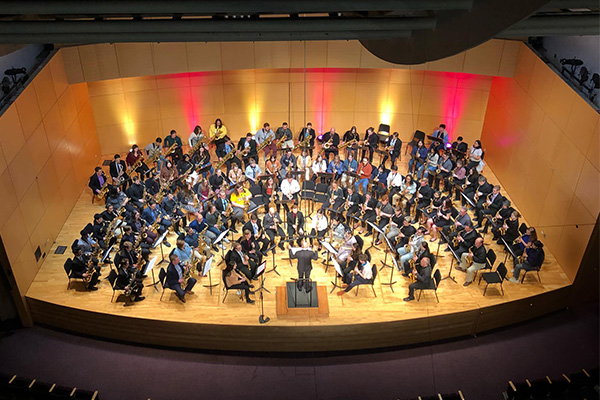 Overhead view of around 100 saxophonists performing on stage at Staples Family Concert Hall