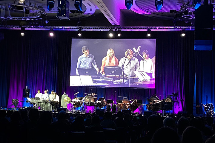 A picture of Landon Schumacker playing percussion on stage with the International Collegiate Percussion Ensemble at the 2023 Percussive Arts Society International Convention