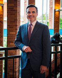 Headshot of Jonathan Nichol. He is standing at the railing of a balcony. You can see a row of upper windows behind him.