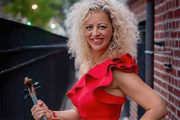 Headshot of Alicia Valoti. She is standing in front of a brick building, holding her viola.