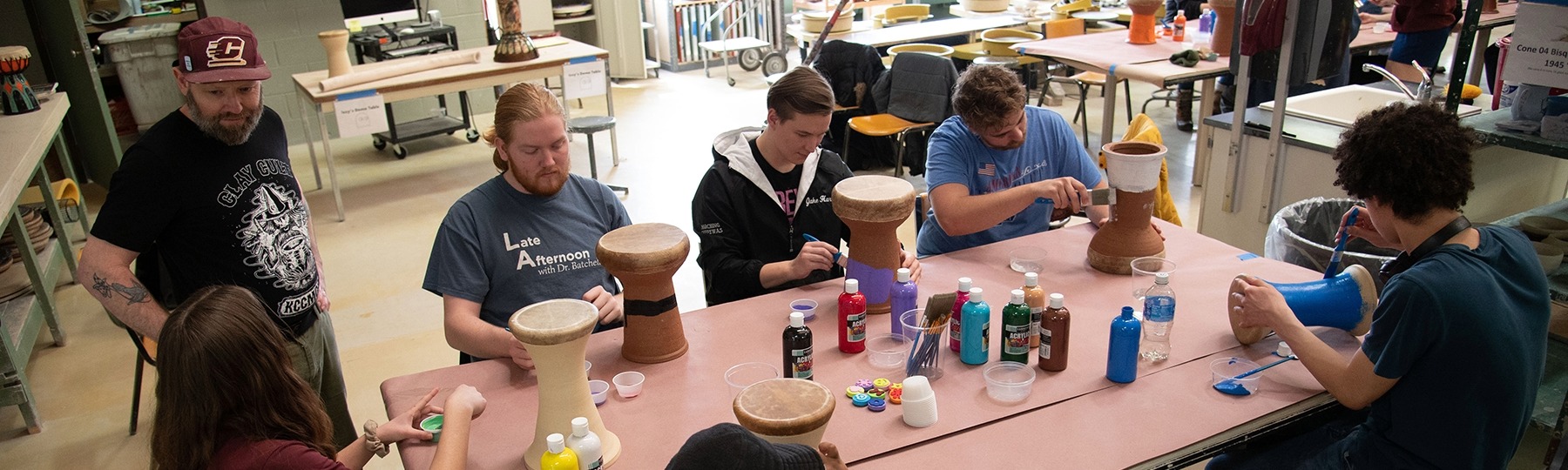 a group of studio arts students painting ceramics at a table