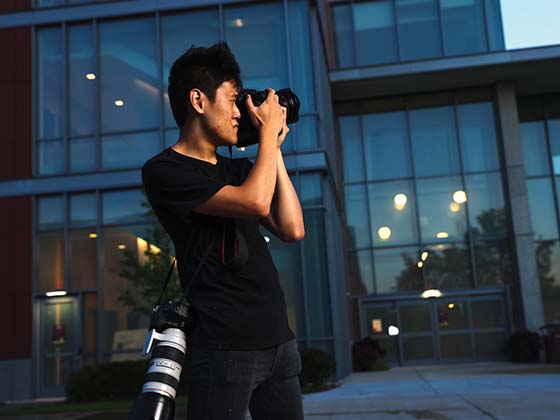 A Photojournalism student at Central Michigan University standing out in front of the Biosciences building on campus to capture a photo.