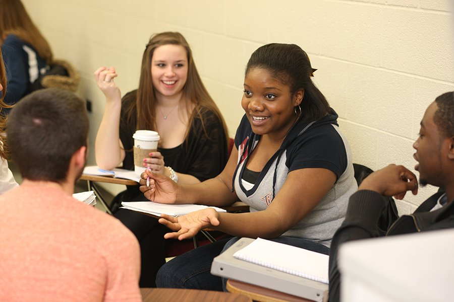 Students sitting in a circle of desks, talking.