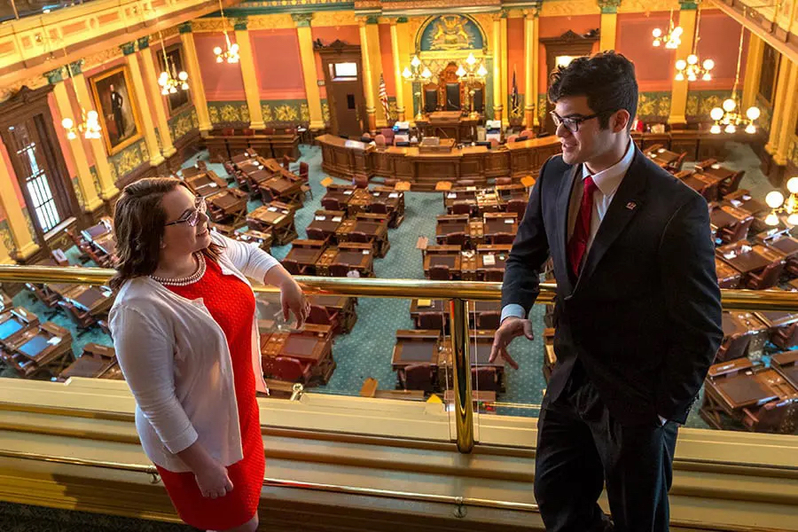 A journalism intern speaks with an employee at the capitol. You can see the capitol room floor laid out behind them.