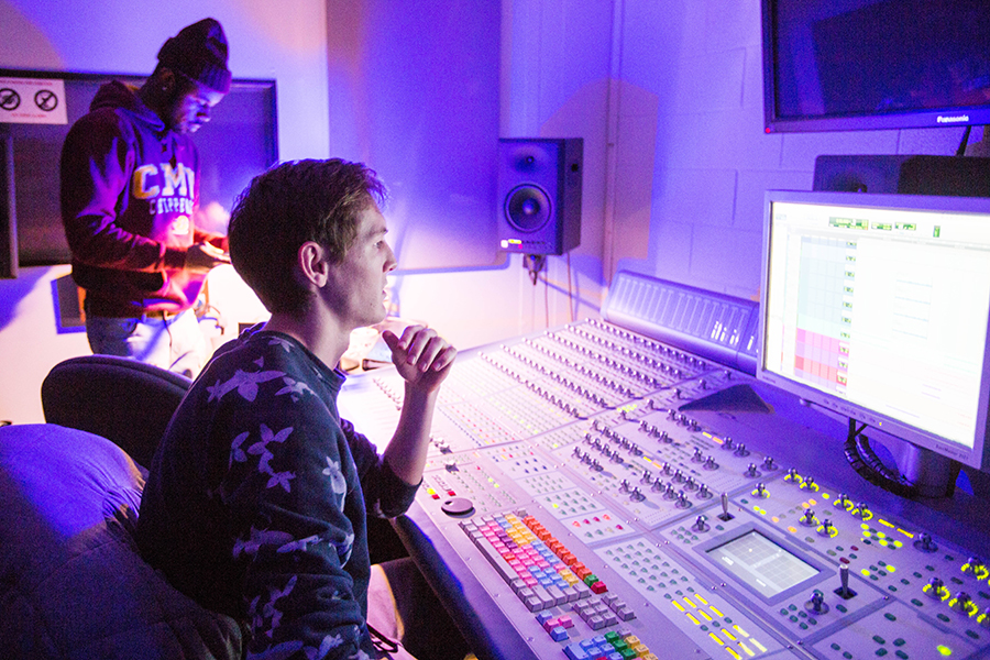 Two students are working on the sound board in the recording studio on campus.