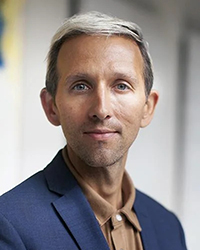Headshot of Andrew Dost. He's wearing a tan shirt with a blue jacket.