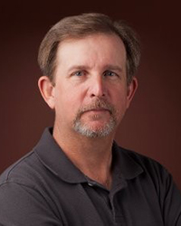 Headshot of Jay Beckman on a brown backdrop.