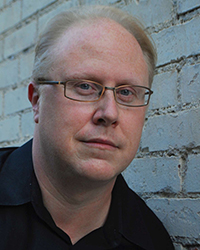 Headshot of Scott Huver in front of a grey brick wall.
