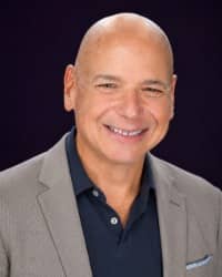 Picture of a man in a gray suit in front of a black background.
