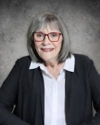 Picture of a woman wearing glasses and a black jacket in front of a gray background.
