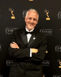 David Parrish in a tuxedo standing in front of a black Emmy Awards backdrop.