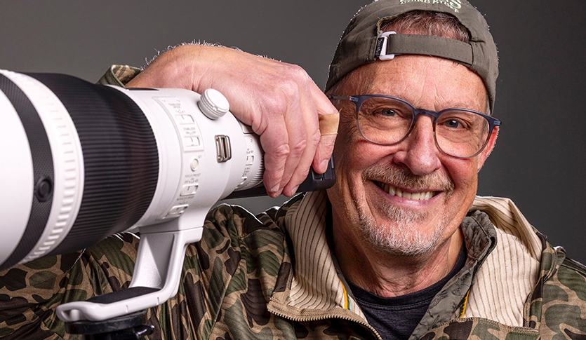 Photographer Steve Jessmore posing with a very large camera lens