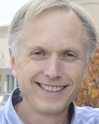 Headshot of Ken Stevens. You can see a house with fall-colored leaves in the background.