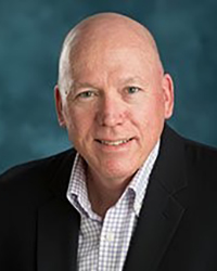 Headshot of Roger Hart on a soft turquoise backdrop.