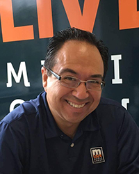Headshot of John Gonzalez in front of a banner for a television station.