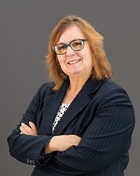 Headshot of Kristina Hajjar wearing a dark blue blazer with arms folded against a soft grey backdrop.