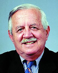 Headshot of David C Smith in a suit and tie in front of a blue backdrop