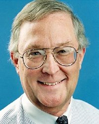 Headshot of Ralph Langer, in a shirt and tie in front of a blue backdrop