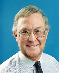 Headshot of Ralph Langer, in a shirt and tie in front of a blue backdrop.