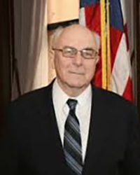 Headshot of Fred Mester in a suit and tie in front of an American flag