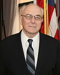 Headshot of Fred Mester in a suit and tie in front of an American flag.