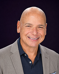 Headshot of Jeff Thomas in a blue polo and grey blazer in front of a black backdrop.