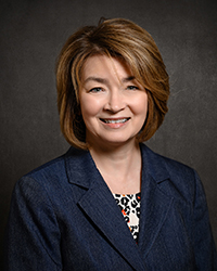 Headshot of Sharon Martin smiling wearing a dark blue blazer in front of a dark grey backdrop.