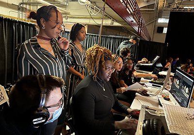 Students from the School of Communication, Journalism, and Media work behind the scenes of the fashion show.