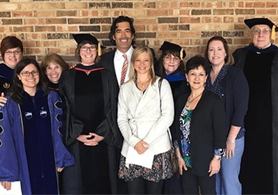 Several graduates pose together for a picture in front of a brick wall.