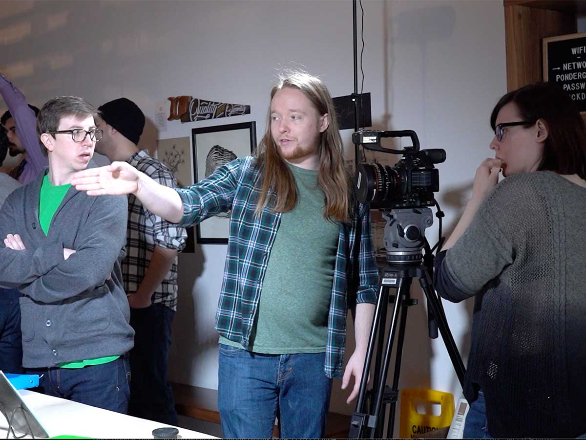 Students in the middle of a film production. One student is behind the camera, another is explaining the scene, while a third is listening to the conversation.